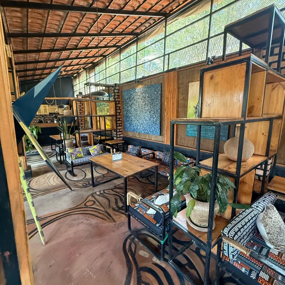 Art-filled lounge with a clay-tile roof, a large blue textured painting on the wall, patterned cushions, open wood-and-steel shelving and swirling black lines painted across the floor